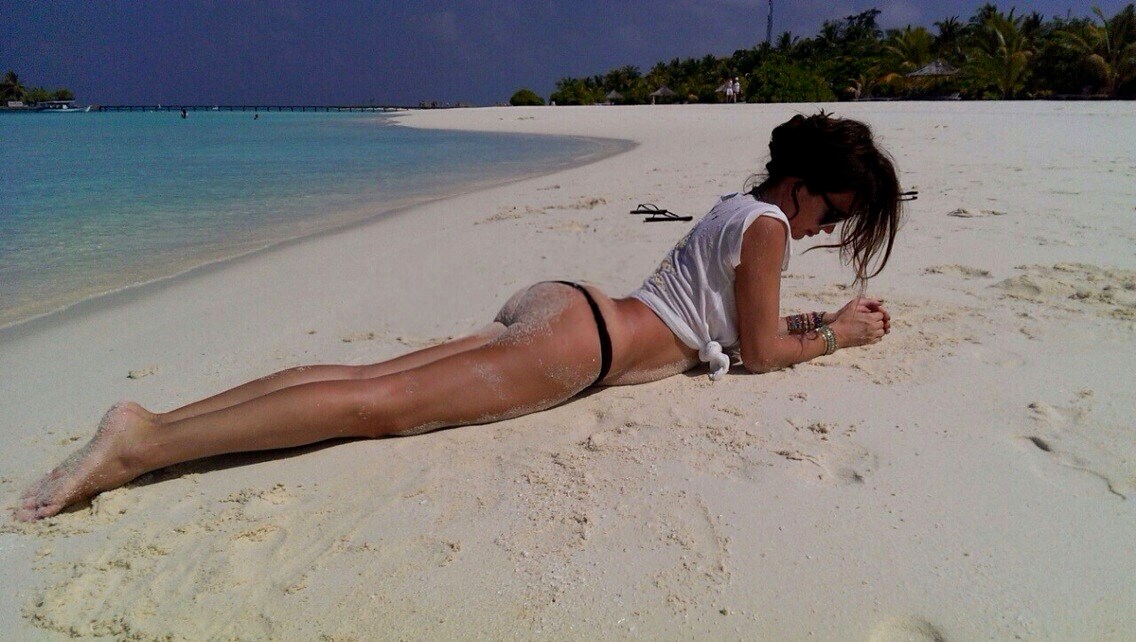 Зрелая женщина в купальнике лежит на пляже и отдыхает попав под камеру